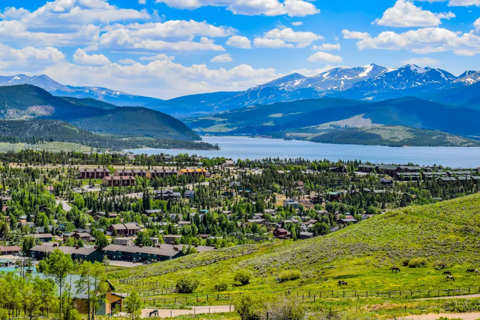 Scenic overlook of town with a lake and snowcapped mountains in the background.